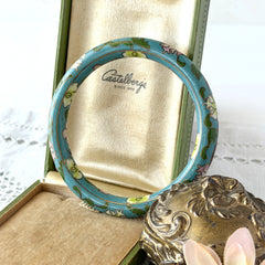 Vintage Chinese turquoise cloisonné bangle with pink and green floral enamel design photographed on linen.