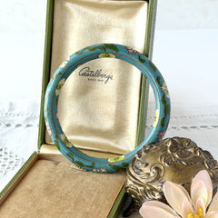 Vintage Chinese turquoise cloisonné bangle with pink and green floral enamel design photographed on linen.