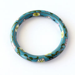 Vintage Chinese turquoise cloisonné bangle with pink and green floral enamel design photographed on linen.