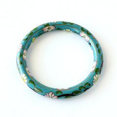 Vintage Chinese turquoise cloisonné bangle with pink and green floral enamel design photographed on linen.
