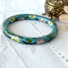Vintage Chinese turquoise cloisonné bangle with pink and green floral enamel design photographed on linen.