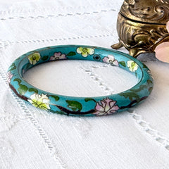 Vintage Chinese turquoise cloisonné bangle with pink and green floral enamel design photographed on linen.