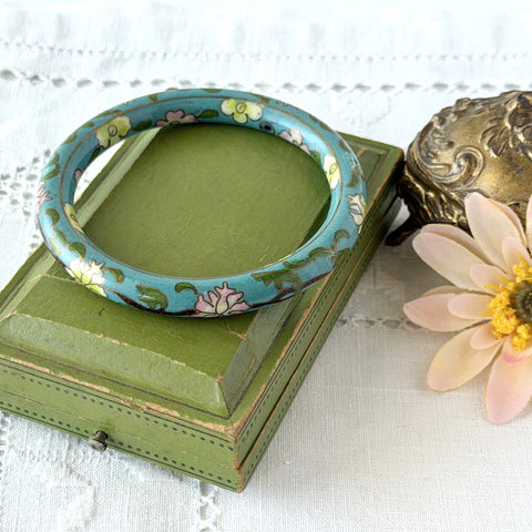 Vintage Chinese turquoise cloisonné bangle with pink and green floral enamel design photographed on linen.