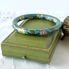 Vintage Chinese turquoise cloisonné bangle with pink and green floral enamel design photographed on linen.