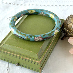 Vintage Chinese turquoise cloisonné bangle with pink and green floral enamel design photographed on linen.