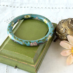 Vintage Chinese turquoise cloisonné bangle with pink and green floral enamel design photographed on linen.