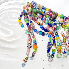 A strand of vintage Chinese lampwork beads from the 1990s, featuring colorful floral and geometric designs in various shapes like oval, cube, and round tube. Each strand includes approximately 20 unique glass beads, new old stock, with a vibrant and playful aesthetic.