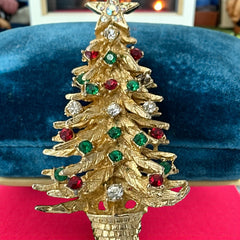 Vintage 1980s gold tone Christmas tree brooch with red, green, and clear rhinestones, featuring a star topper and woven basket base; shown from multiple angles to highlight dimensional detail, condition, and clasp.