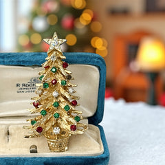 Vintage 1980s gold tone Christmas tree brooch with red, green, and clear rhinestones, featuring a star topper and woven basket base; shown from multiple angles to highlight dimensional detail, condition, and clasp.