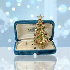 Vintage 1980s gold tone Christmas tree brooch with red, green, and clear rhinestones, featuring a star topper and woven basket base; shown from multiple angles to highlight dimensional detail, condition, and clasp.