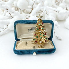 Vintage 1980s gold tone Christmas tree brooch with red, green, and clear rhinestones, featuring a star topper and woven basket base; shown from multiple angles to highlight dimensional detail, condition, and clasp.