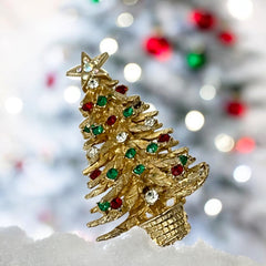 Vintage 1980s gold tone Christmas tree brooch with red, green, and clear rhinestones, featuring a star topper and woven basket base; shown from multiple angles to highlight dimensional detail, condition, and clasp.