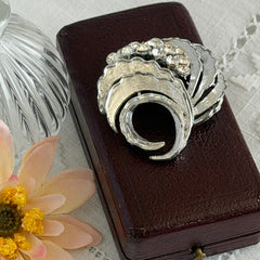 Vintage silver tone swirl leaf brooch with clear rhinestone cluster, textured metal, 1970s–1980s.