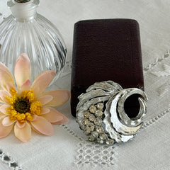 Vintage silver tone swirl leaf brooch with clear rhinestone cluster, textured metal, 1970s–1980s.