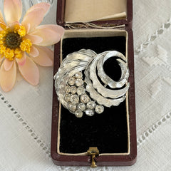 Vintage silver tone swirl leaf brooch with clear rhinestone cluster, textured metal, 1970s–1980s.