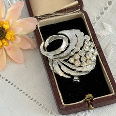 Vintage silver tone swirl leaf brooch with clear rhinestone cluster, textured metal, 1970s–1980s.
