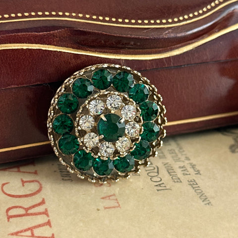 Vintage Coro round brooch with layered emerald green and clear rhinestones in a gold‑tone setting, signed on the back with a standard pin clasp and light vintage wear.