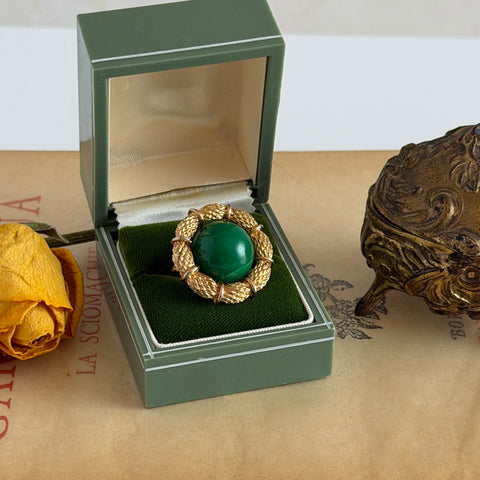 Vintage Coro gold‑tone ring with a round green cabochon set in a textured frame, with soft light highlighting the details.