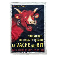 Coucke tea towel featuring a vintage advertisement of La Vache qui Rit, illustrated by Benjamin Rabier. The design shows the iconic red laughing cow with cheese box earrings on a black background, with French text promoting luxury cream of gruyère. Made of 100% cotton.