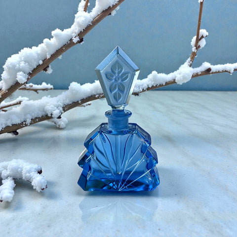 Vintage Czech Art Deco sapphire blue fan‑shaped perfume bottle with geometric stopper and frosted intaglio floral dauber, shown in styled settings that highlight its faceted design, vibrant color, and collectible craftsmanship.