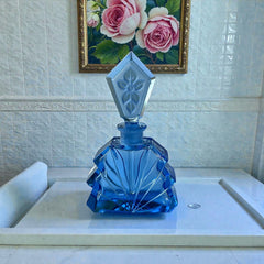 Vintage Czech Art Deco sapphire blue fan‑shaped perfume bottle with geometric stopper and frosted intaglio floral dauber, shown in styled settings that highlight its faceted design, vibrant color, and collectible craftsmanship.