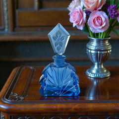 Vintage Czech Art Deco sapphire blue fan‑shaped perfume bottle with geometric stopper and frosted intaglio floral dauber, shown in styled settings that highlight its faceted design, vibrant color, and collectible craftsmanship.
