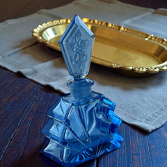 Vintage Czech Art Deco sapphire blue fan‑shaped perfume bottle with geometric stopper and frosted intaglio floral dauber, shown in styled settings that highlight its faceted design, vibrant color, and collectible craftsmanship.