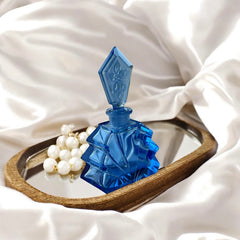 Vintage Czech Art Deco sapphire blue fan‑shaped perfume bottle with geometric stopper and frosted intaglio floral dauber, shown in styled settings that highlight its faceted design, vibrant color, and collectible craftsmanship.