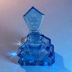 Vintage Czech Art Deco sapphire blue fan‑shaped perfume bottle with geometric stopper and frosted intaglio floral dauber, shown in styled settings that highlight its faceted design, vibrant color, and collectible craftsmanship.