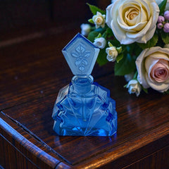Vintage Czech Art Deco sapphire blue fan‑shaped perfume bottle with geometric stopper and frosted intaglio floral dauber, shown in styled settings that highlight its faceted design, vibrant color, and collectible craftsmanship.