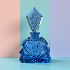 Vintage Czech Art Deco sapphire blue fan‑shaped perfume bottle with geometric stopper and frosted intaglio floral dauber, shown in styled settings that highlight its faceted design, vibrant color, and collectible craftsmanship.