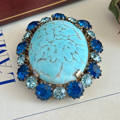 Vintage Czech statement brooch featuring a large faux turquoise Hubbell glass oval cabochon surrounded by alternating capri blue and light sapphire rhinestones in a gold‑tone prong‑set setting, shown from various angles.