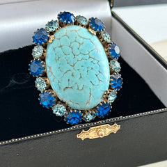 Vintage Czech statement brooch featuring a large faux turquoise Hubbell glass oval cabochon surrounded by alternating capri blue and light sapphire rhinestones in a gold‑tone prong‑set setting, shown from various angles.