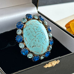 Vintage Czech statement brooch featuring a large faux turquoise Hubbell glass oval cabochon surrounded by alternating capri blue and light sapphire rhinestones in a gold‑tone prong‑set setting, shown from various angles.