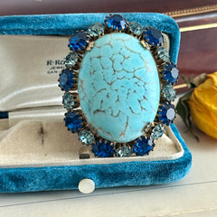 Vintage Czech statement brooch featuring a large faux turquoise Hubbell glass oval cabochon surrounded by alternating capri blue and light sapphire rhinestones in a gold‑tone prong‑set setting, shown from various angles.