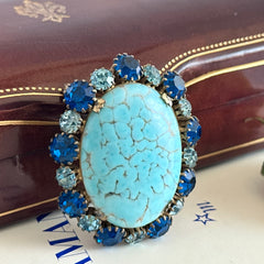 Vintage Czech statement brooch featuring a large faux turquoise Hubbell glass oval cabochon surrounded by alternating capri blue and light sapphire rhinestones in a gold‑tone prong‑set setting, shown from various angles.