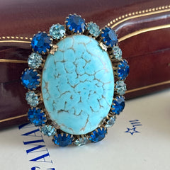 Vintage Czech statement brooch featuring a large faux turquoise Hubbell glass oval cabochon surrounded by alternating capri blue and light sapphire rhinestones in a gold‑tone prong‑set setting, shown from various angles.