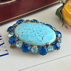 Vintage Czech statement brooch featuring a large faux turquoise Hubbell glass oval cabochon surrounded by alternating capri blue and light sapphire rhinestones in a gold‑tone prong‑set setting, shown from various angles.