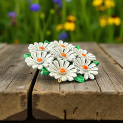 Vintage 1960s enamel daisy brooch with white petals, orange centers, and green leaves in a round floral cluster. Silver-toned finish, 2-inch diameter, in very good condition.