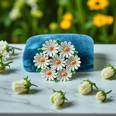 Vintage 1960s enamel daisy brooch with white petals, orange centers, and green leaves in a round floral cluster. Silver-toned finish, 2-inch diameter, in very good condition.