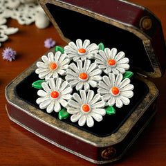 Vintage 1960s enamel daisy brooch with white petals, orange centers, and green leaves in a round floral cluster. Silver-toned finish, 2-inch diameter, in very good condition.