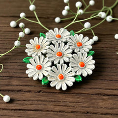 Vintage 1960s enamel daisy brooch with white petals, orange centers, and green leaves in a round floral cluster. Silver-toned finish, 2-inch diameter, in very good condition.