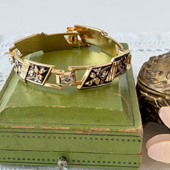 Vintage Spanish damascene gold‑tone bracelet with black enamel floral links, silver inlay, and red rhinestone accents, shown in various angles highlighting its 1960s Toledo craftsmanship and slide clasp with safety chain.