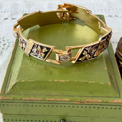 Vintage Spanish damascene gold‑tone bracelet with black enamel floral links, silver inlay, and red rhinestone accents, shown in various angles highlighting its 1960s Toledo craftsmanship and slide clasp with safety chain.