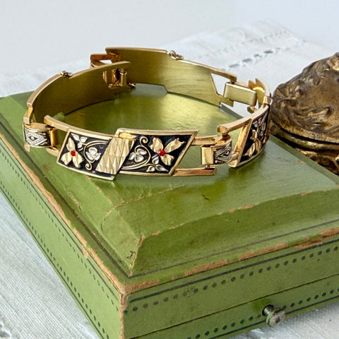Vintage Spanish damascene gold‑tone bracelet with black enamel floral links, silver inlay, and red rhinestone accents, shown in various angles highlighting its 1960s Toledo craftsmanship and slide clasp with safety chain.