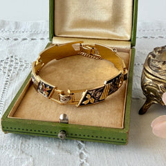 Vintage Spanish damascene gold‑tone bracelet with black enamel floral links, silver inlay, and red rhinestone accents, shown in various angles highlighting its 1960s Toledo craftsmanship and slide clasp with safety chain.