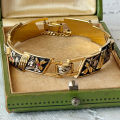 Vintage Spanish damascene gold‑tone bracelet with black enamel floral links, silver inlay, and red rhinestone accents, shown in various angles highlighting its 1960s Toledo craftsmanship and slide clasp with safety chain.