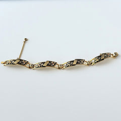 Vintage Spanish damascene gold‑tone bracelet with black enamel floral links, silver inlay, and red rhinestone accents, shown in various angles highlighting its 1960s Toledo craftsmanship and slide clasp with safety chain.