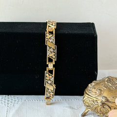 Vintage Spanish damascene gold‑tone bracelet with black enamel floral links, silver inlay, and red rhinestone accents, shown in various angles highlighting its 1960s Toledo craftsmanship and slide clasp with safety chain.