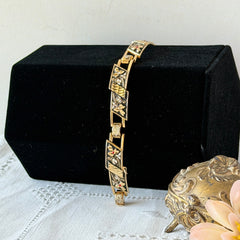 Vintage Spanish damascene gold‑tone bracelet with black enamel floral links, silver inlay, and red rhinestone accents, shown in various angles highlighting its 1960s Toledo craftsmanship and slide clasp with safety chain.